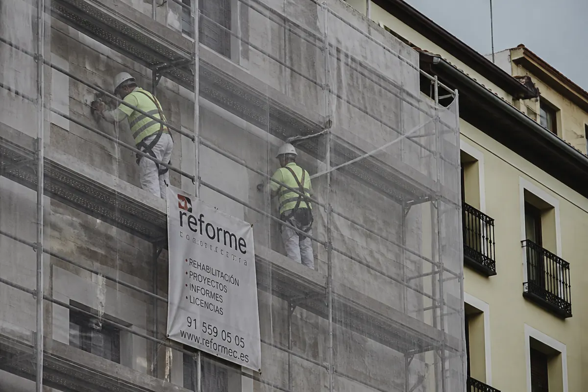 Operarios con EPI retiran revestimiento inestable desde andamio con redes de protección en fachada urbana