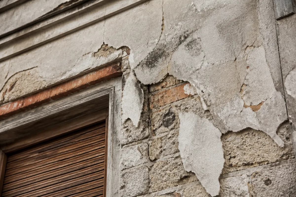 Detalle de fachada residencial con fisuras y revestimiento deteriorado bajo luz natural, encuadre cercano