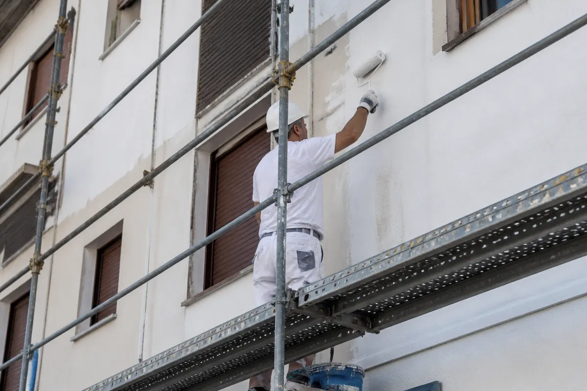 Operario pinta fachada desde andamio protegido tras saneado del revestimiento en edificio residencial